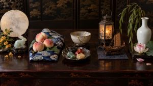 A symbolic still life with a moon and rabbit, peaches, repair stones, a maritime lantern and boat, and a willow vase